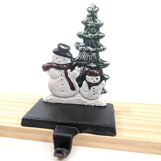 Cast iron Christmas stocking holder featuring two snowmen with red scarves beside a Christmas tree in a winter wonderland scene